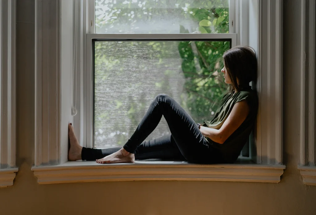 Mujer sentada en el alféizar de una ventana, tranquila, mirando hacia fuera
